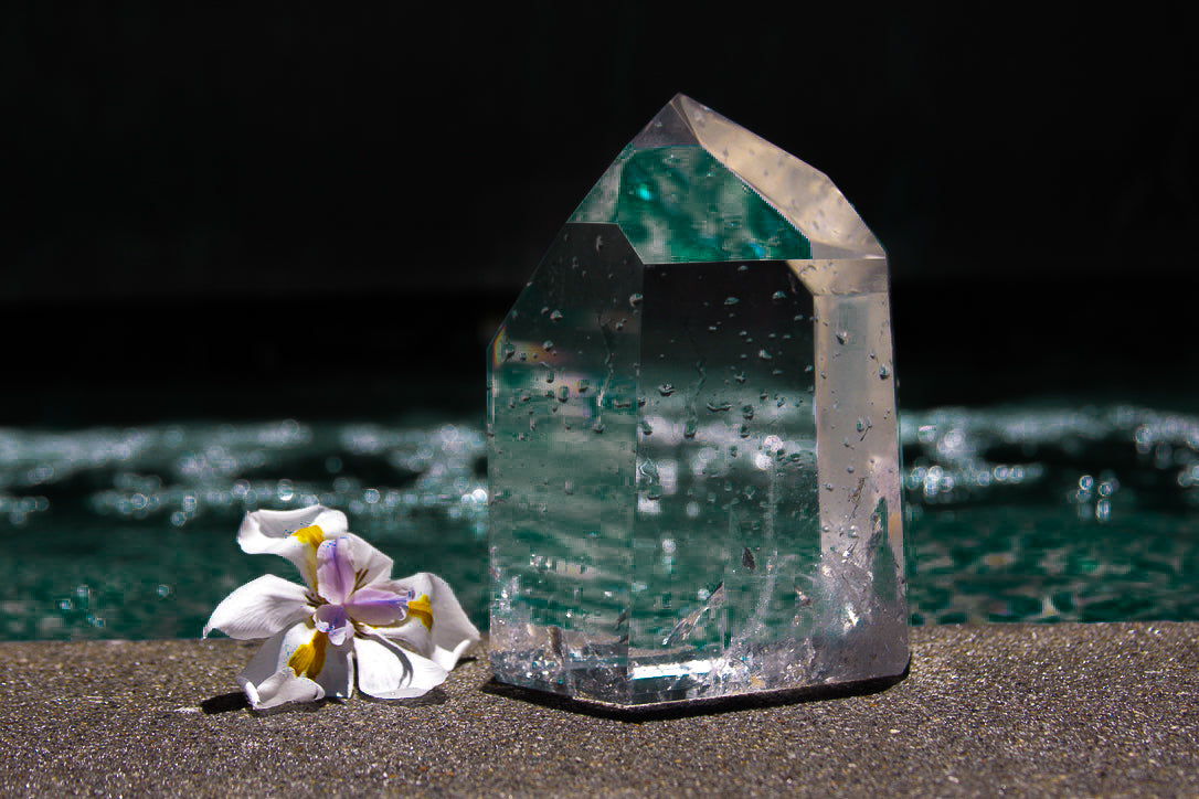 Clear polished quartz tower beside a white flower by a pool
