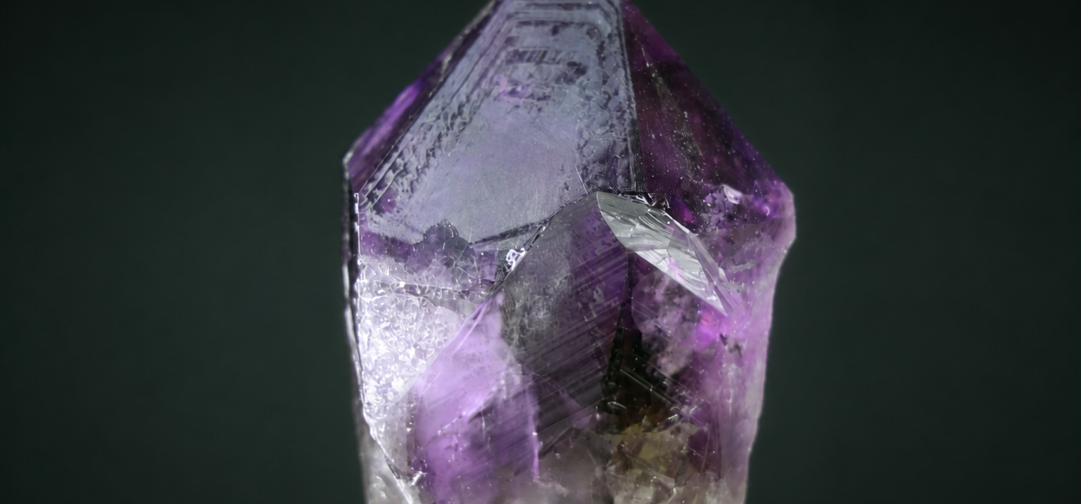 Natural amethyst point with triangular growth markings against a deep green background