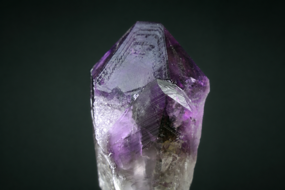 Natural amethyst point with triangular growth markings against a deep green background