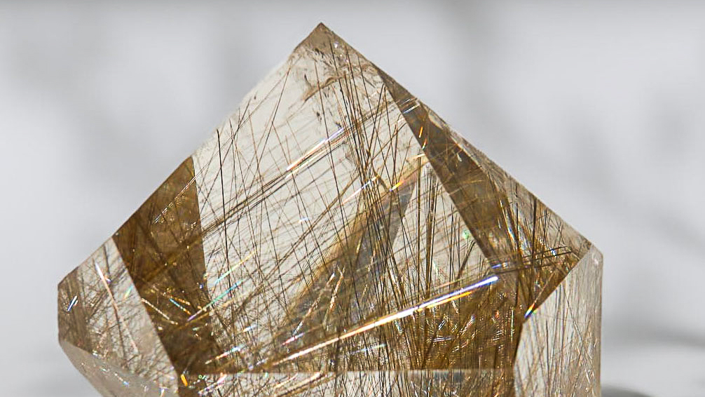 Polished rutilated quartz freeform with dense natural rutile needles against a neutral background