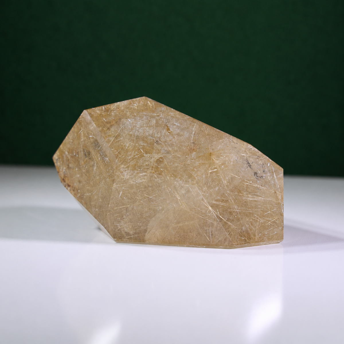 Polished rutilated quartz freeform, 1.258 kg, main view on a white surface with a dark green background.