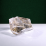 Polished rutilated quartz freeform, 271 g, main view on a white surface with a dark green background.