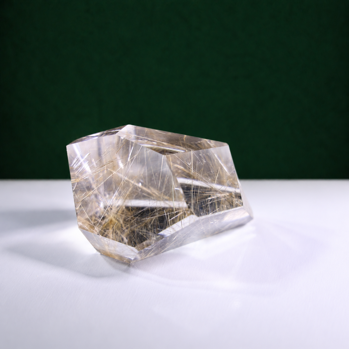 Polished rutilated quartz freeform, 271 g, main view on a white surface with a dark green background.