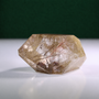 Polished rutilated quartz freeform, 417 g, front view on a white surface with a dark green background.