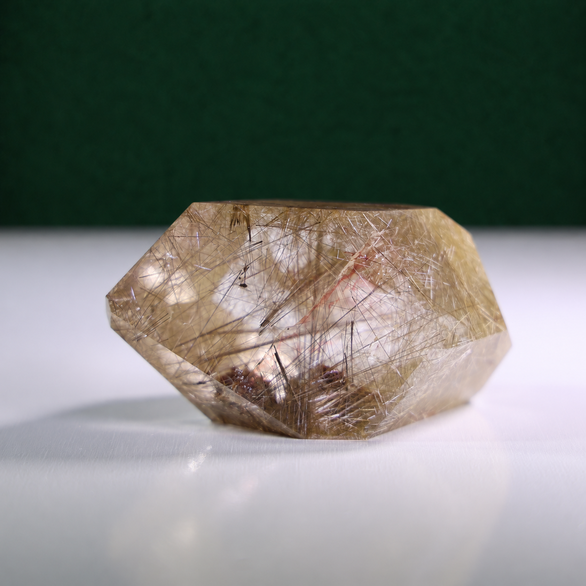 Polished rutilated quartz freeform, 417 g, front view on a white surface with a dark green background.