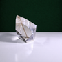 Polished rutilated quartz freeform, 72 g, main view on a white surface with a dark green background.