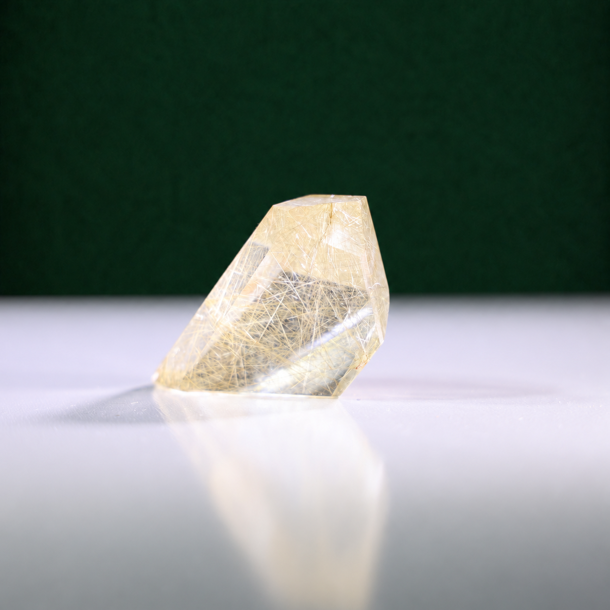 Polished rutilated quartz freeform, 79 g, main view on a white surface with a dark green background.