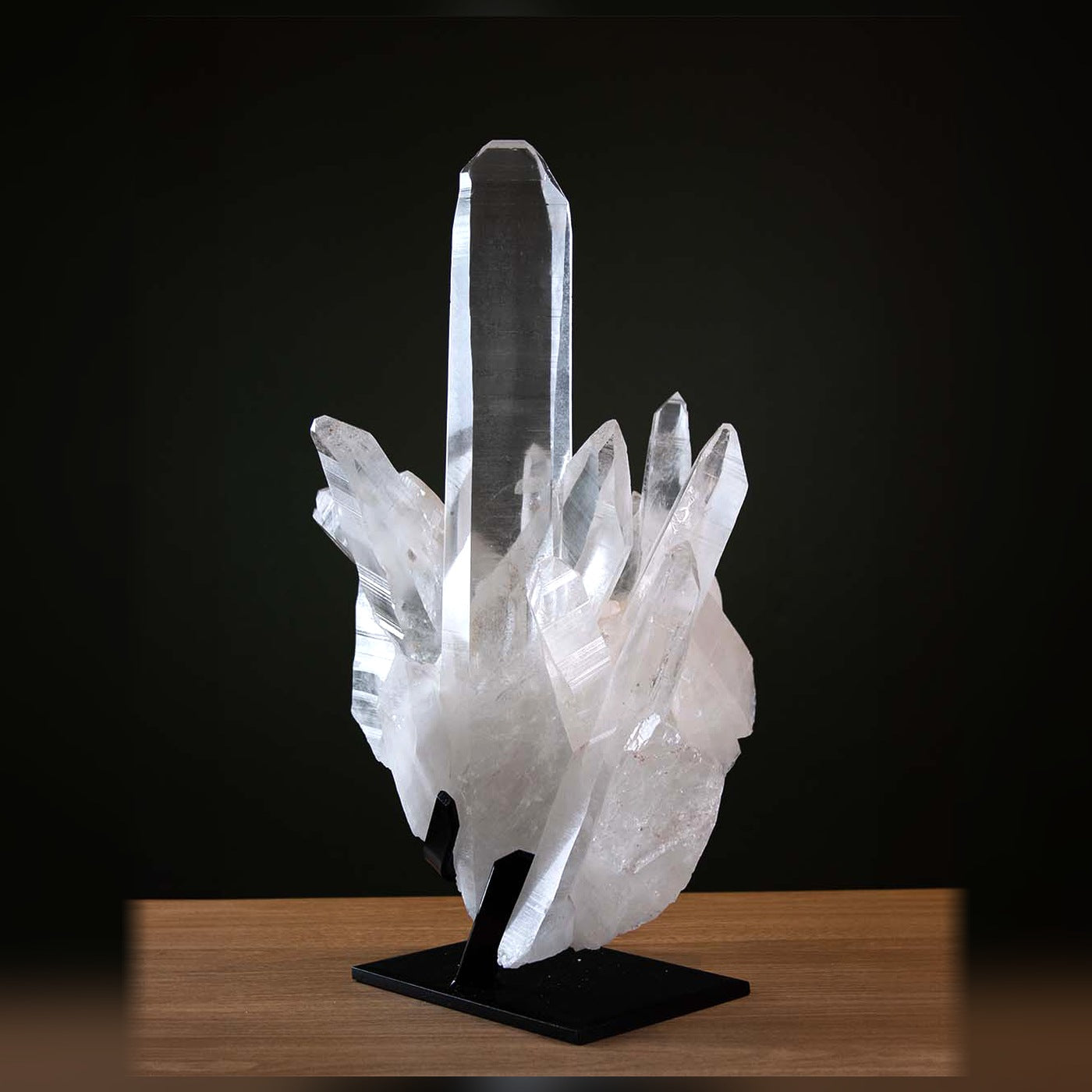 Tall clear quartz cluster displayed on a black stand against a dark green background.